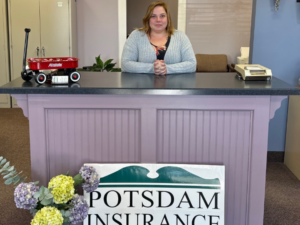 Markel smiling while sitting at the reception with Potsdam Insurance Agency sign.